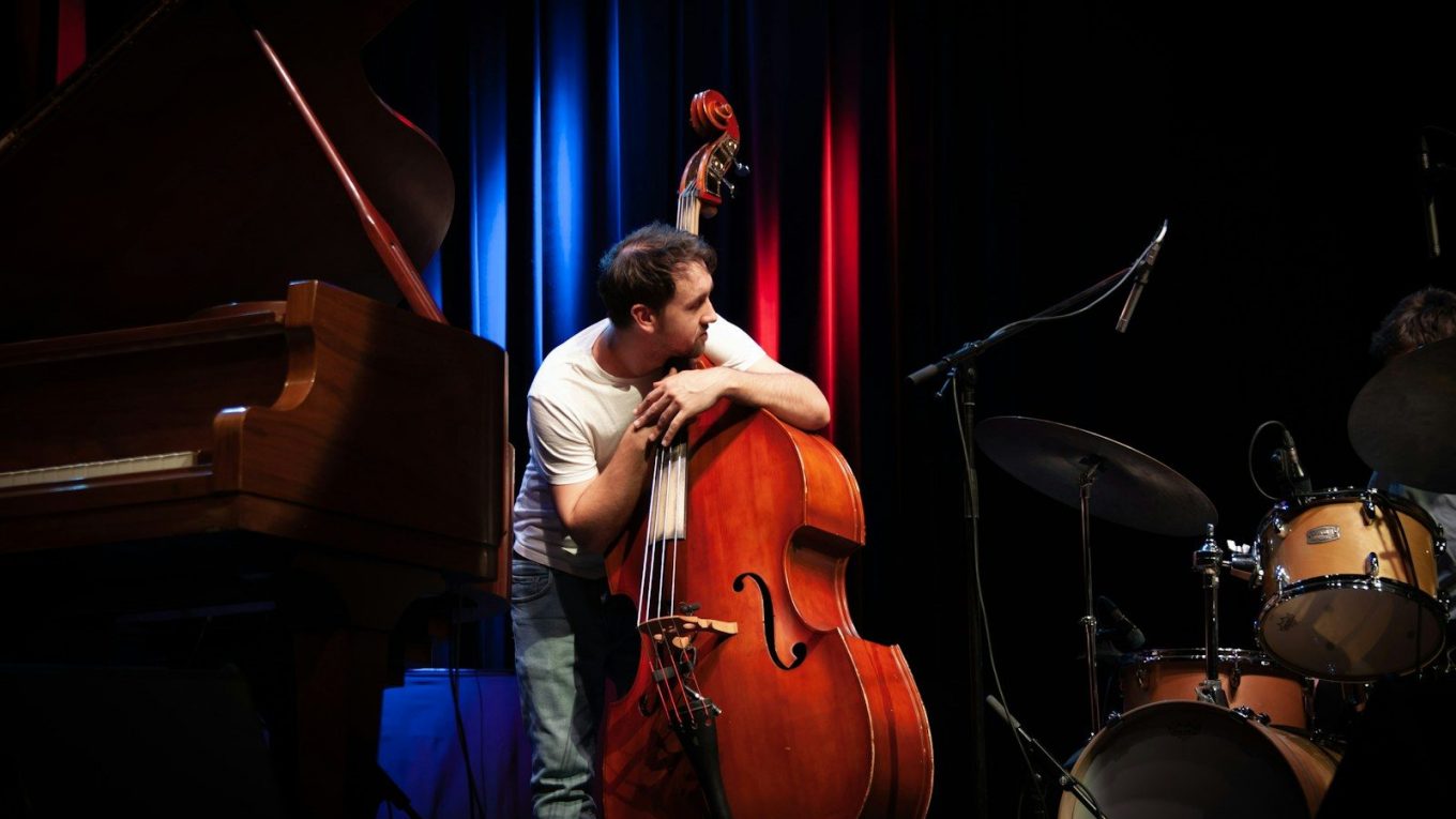 a man holding a cello while standing next to a piano