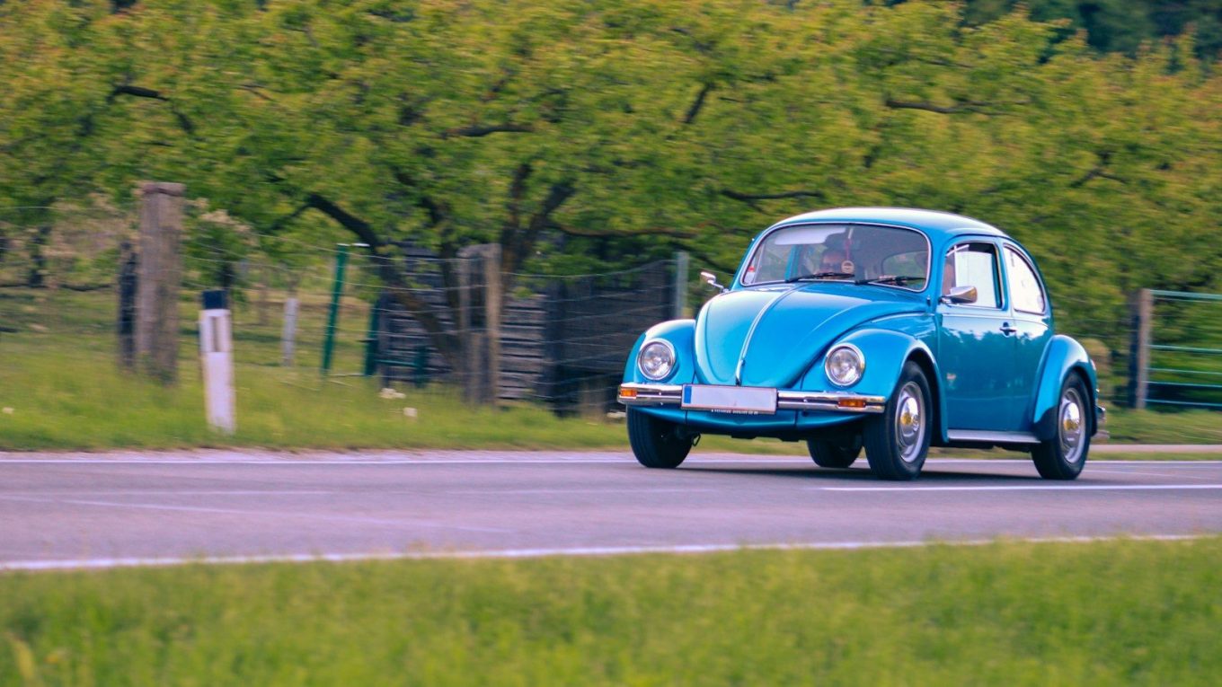 A blue volkswagen beetle drives on a road